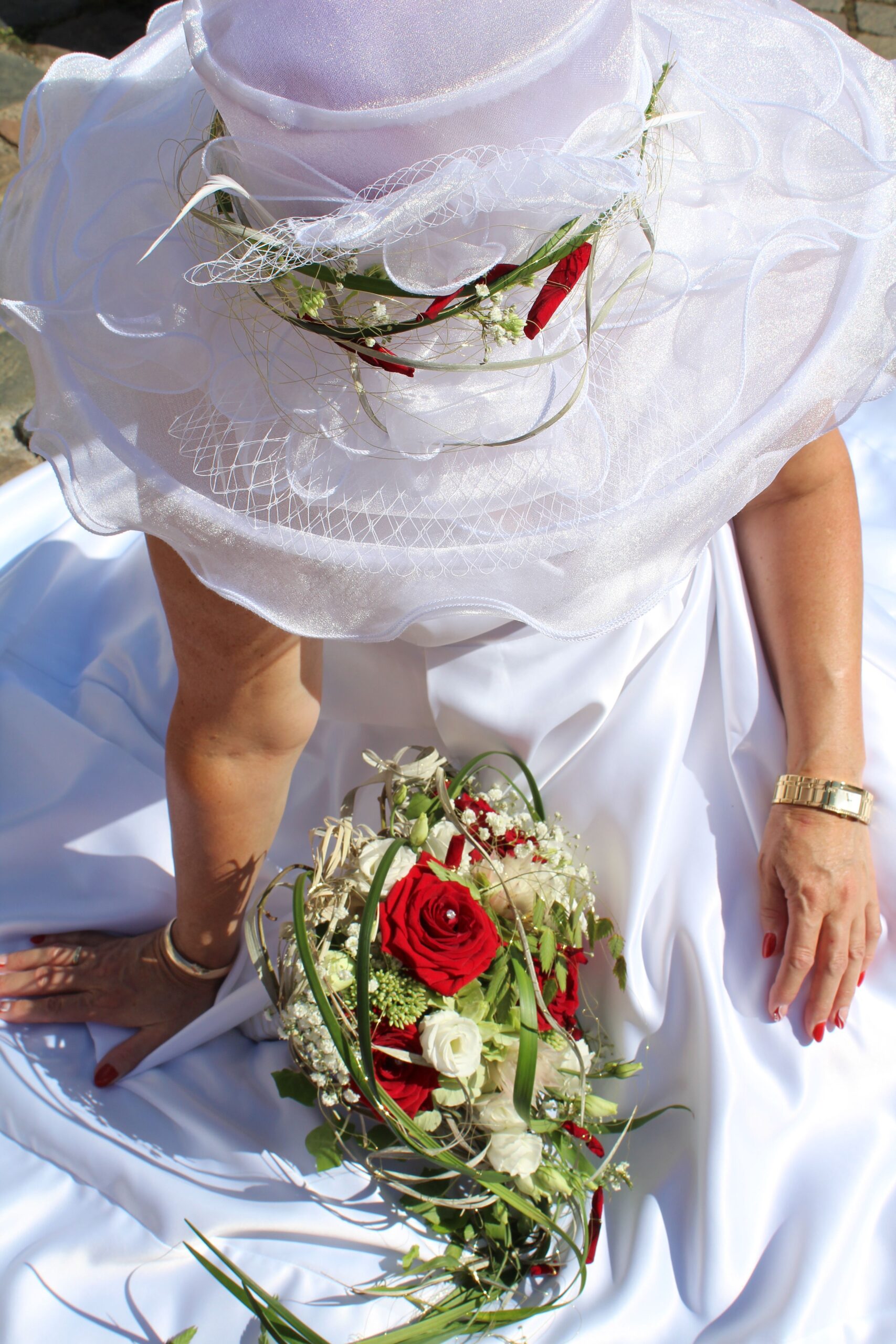 A bride in white dress and hat holding a beautiful bouquet of roses.