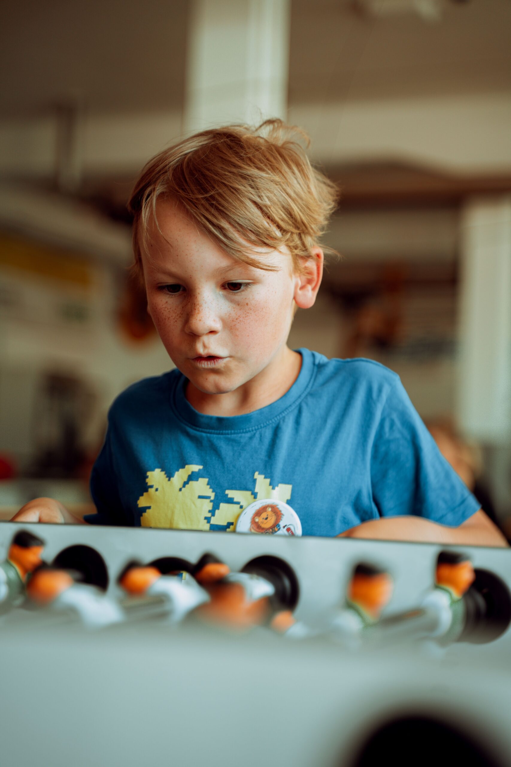 Kinder- und Familienfotos A young boy intensely focused on a foosball game indoors. Captivated expression enhances the playful setting.
