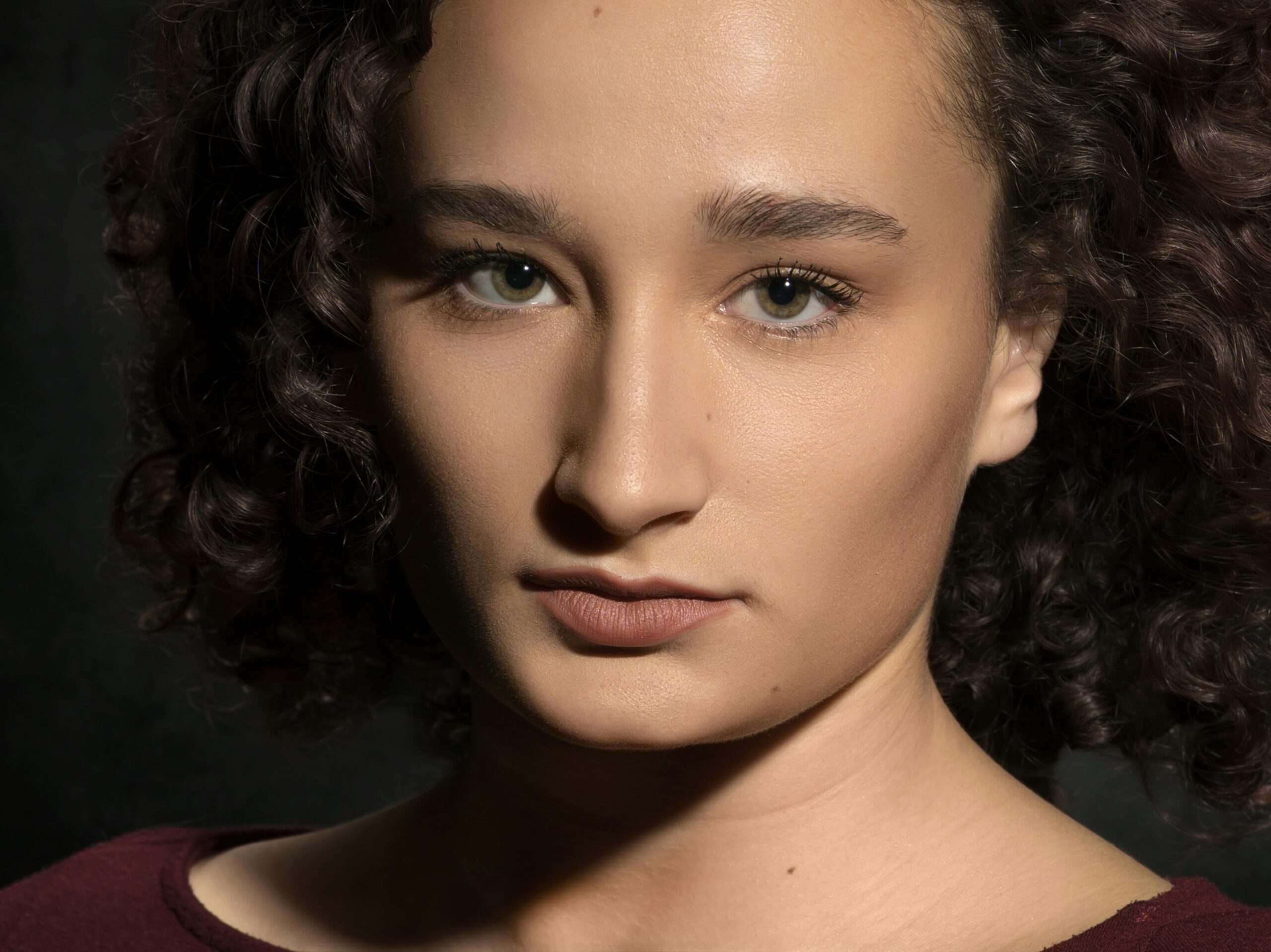 Portraits A striking close-up portrait capturing a woman with curly hair against a dark background.